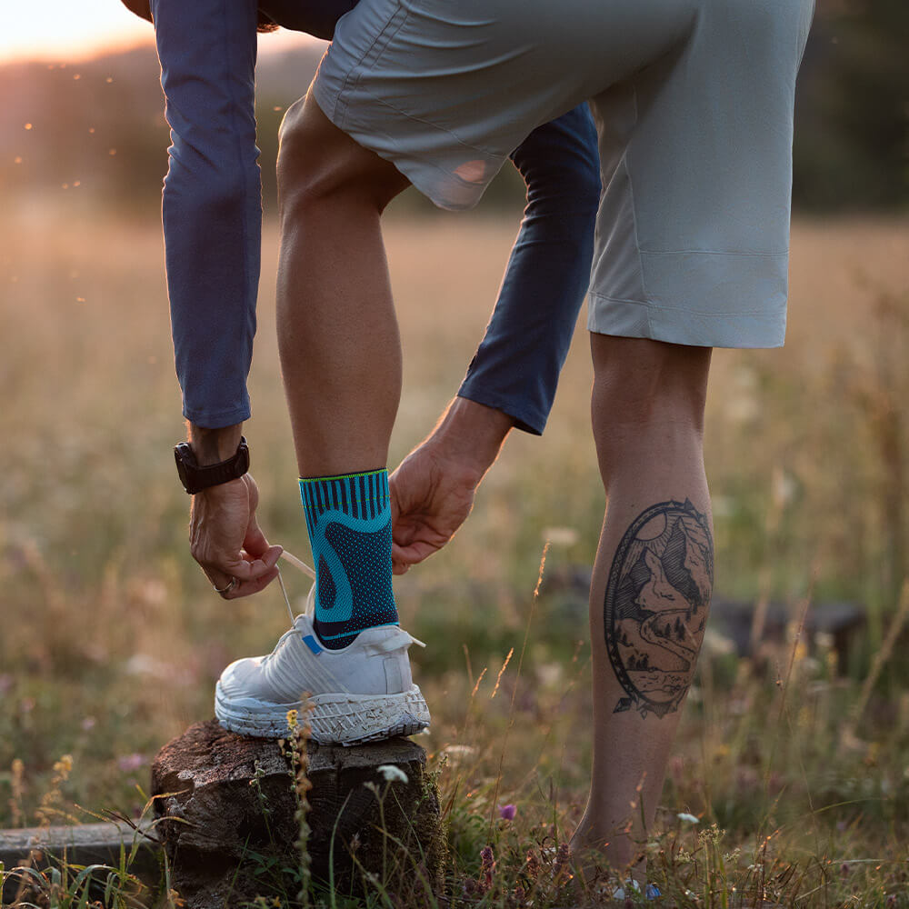 Ein Mann stellt seinen Fuß auf einen Baumstumpf und bindet sein Schuh neu	 er hat eine Achillessehnenbandage am linken Fuß