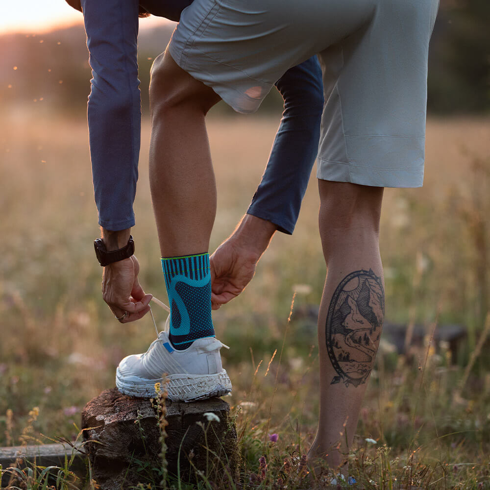 Achillessehnenbandage rivera Outdoor Ein Mann stellt seinen Fuß auf einen Baumstumpf und bindet sein Schuh neu	 er hat eine Achillessehnenbandage am linken Fuß