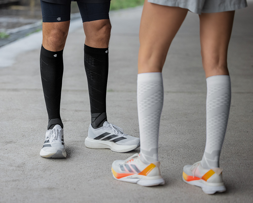 In voller Pracht: unsere Run Performance Compression Socks in ihrem Element Unterschenkel eines Läufers in Nahaufnahme mit blau gemusterten Laufsocken auf einem Betonuntergrund