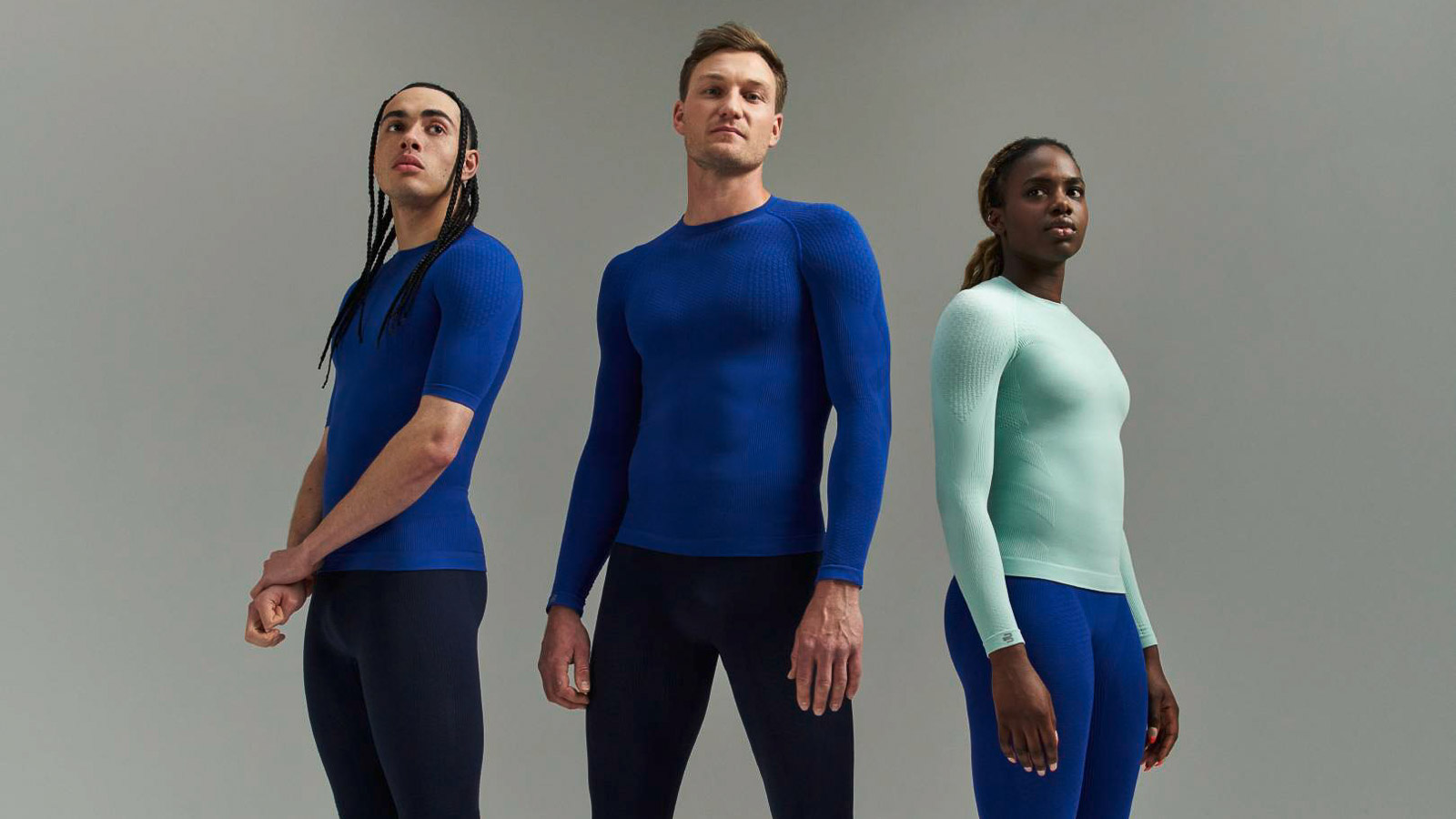 Drei Athleten in Sportbekleidung mit Kompressions-Shirts und Kompressionshosen vor grauem Hintergrund.