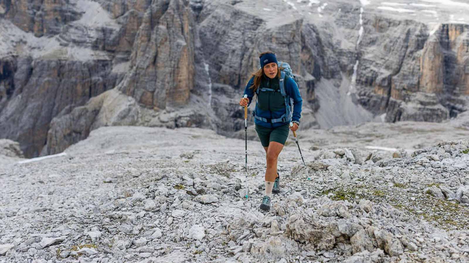 Eine fordernde aber schöne Wanderung in den Dolomiten Eine Wanderin in den Dolomiten läüft mit Stöcken über ein Steinfeld und trägt eine Wander Bandage.