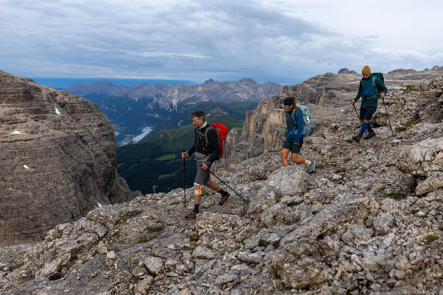 Wandern mit Aussicht in den Dolomiten Drei Personen auf einer Wanderung in den Dolomiten, die über ein Steinfeld wandern und ein Blick ins grüne Tal haben können.