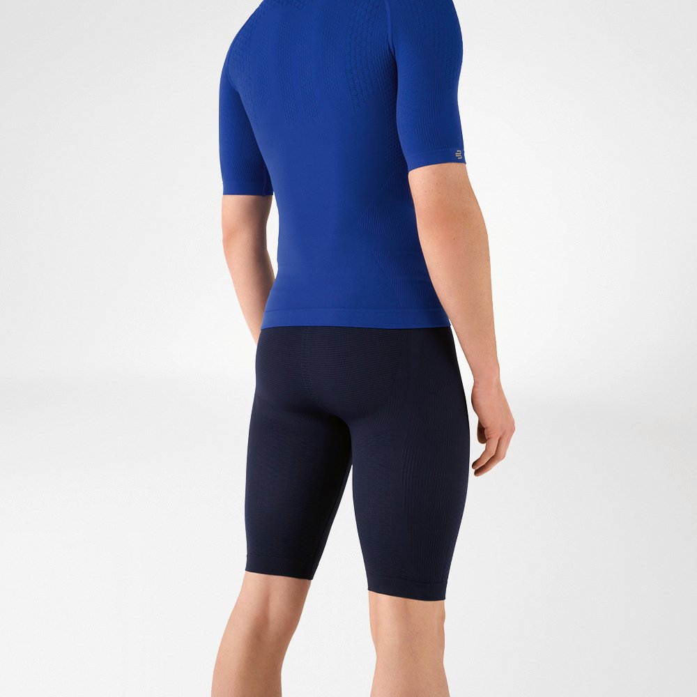 Der Mann trägt ein eng anliegendes, blaues Shirt, das seinen Oberkörper betont, sowie eine knielange, marineblaue, eng geschnittene Sporthose, die seinen Unterkörper umschließt.