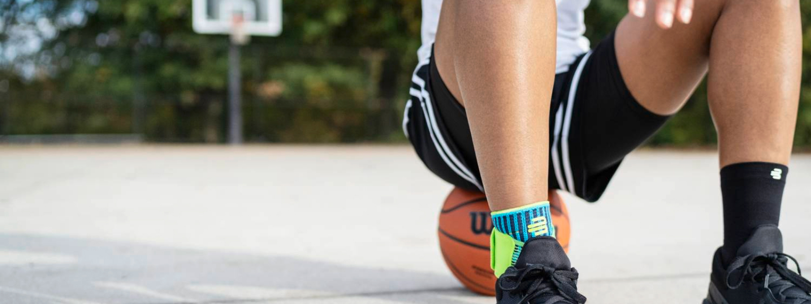 Streetball Basketballspieler mit Knöchel Bandage Streetball-Spieler mit Fußbandage sitzt auf einem Basketball auf einem Streetcourt-Feld