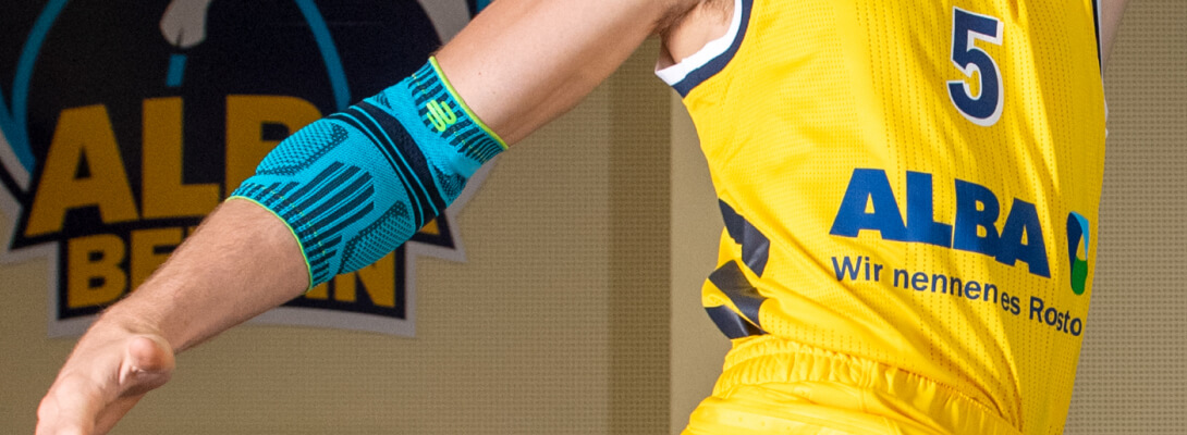 Ellenbogenbandage beim Basketball Basketballspieler mit Alba Berlin Trikot trägt eine Sportsbandage für den Ellenbogen