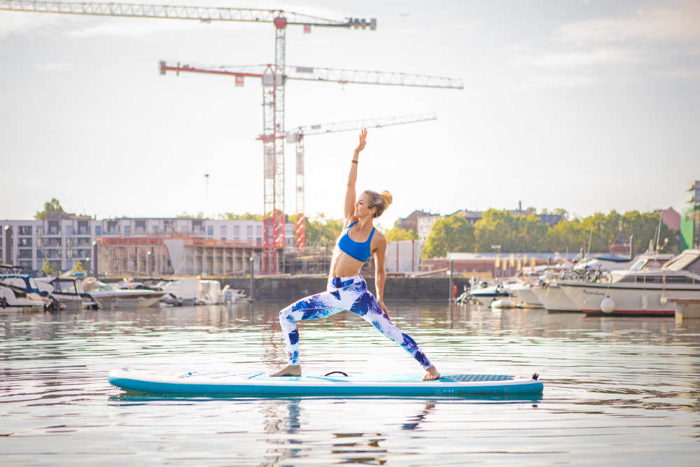 SUP Yoga - spektakulär und effizient Frau macht Yoga auf dem Wasser: Auf den Händen stehend Bein nach oben