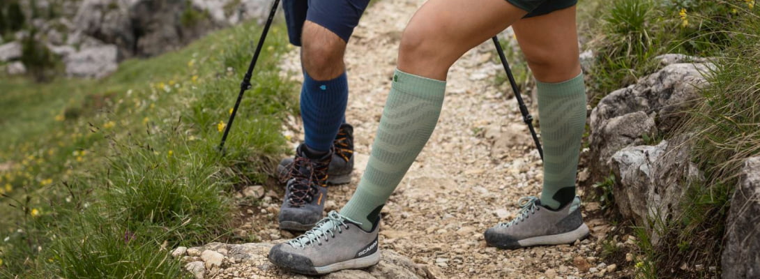 Zwei Personen wandern über Felsen	 sie tragen Merino-Wandersocken	 im Hintergrund sind Bäume zu sehen