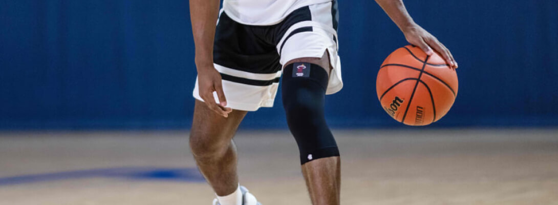 Alles im Griff mit der unserer Compression Knee Support Detailbild Basketballspieler mit einem Basketball in der Hand trägt einen schwarzen NBA Knee Sleeve