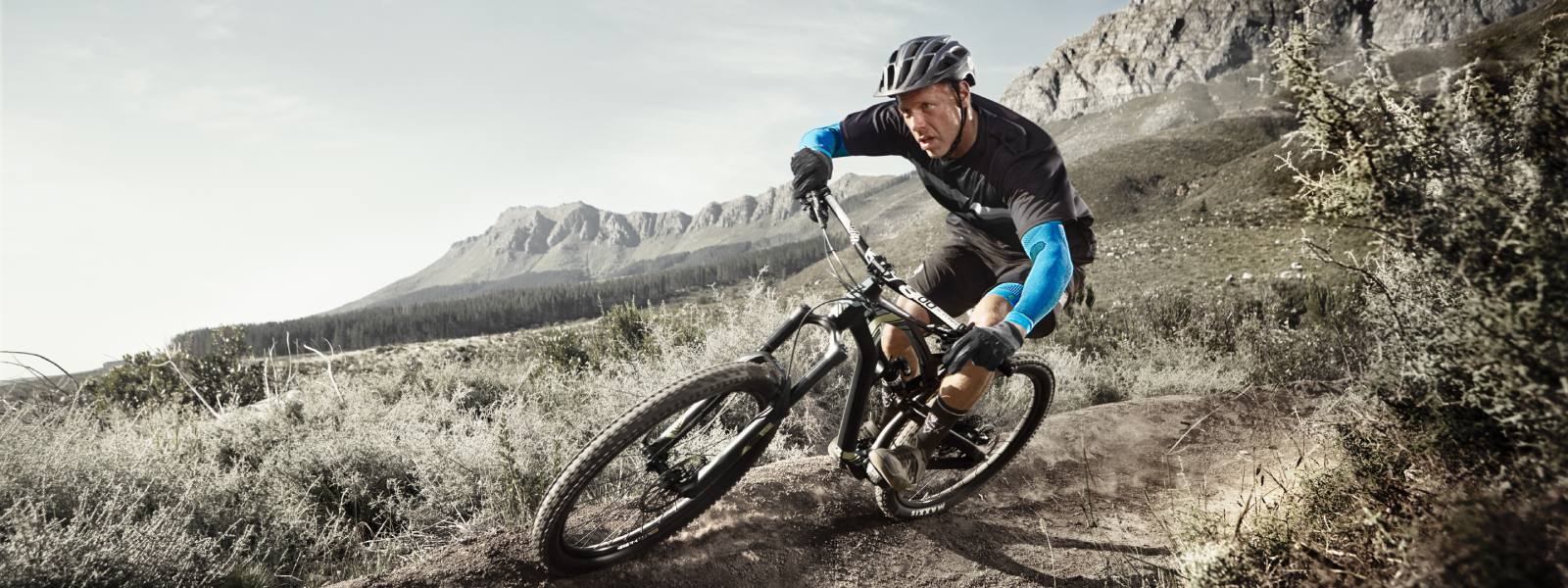 Mountainbiken mit Arm Sleeves Mountainbiker fährt einen Hang herunter und trägt dabei blaue Arm Sleeves