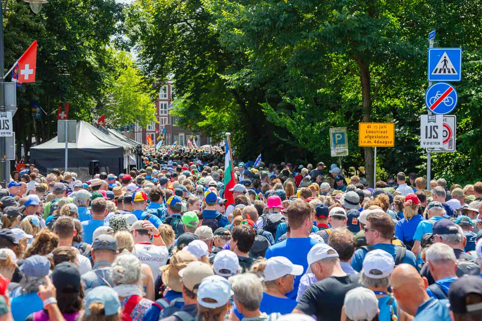 Dichte Menschenmenge von Wanderern beim 4Daagse in Nijmegen, unterwegs durch die Straßen mit Flaggen, Schildern und sommerlicher Atmosphäre.