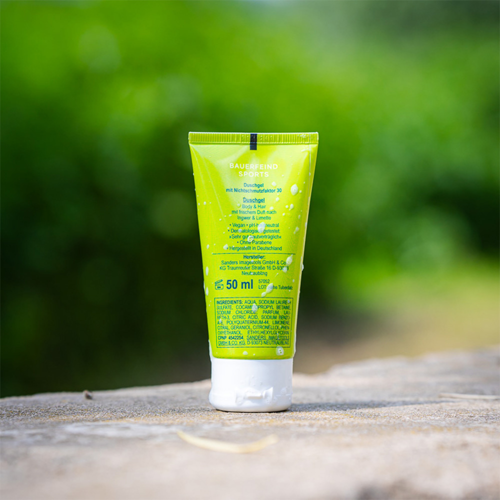 Natürliche Pflege: Inhaltsstoffe des Bauerfeind Sports ShowerPower Duschgels Rückansicht der grünen Bauerfeind Sports Duschgel-Tube "ShowerPower" mit Inhaltsangaben und Produktinformationen. Die Tube steht auf einem Stein im Freien.