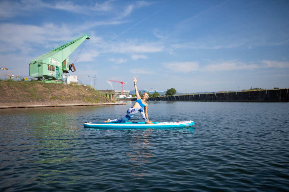 SUP Yoga - einfach mal treiben lassen Frau macht Yoga-Übung auf dem Board mit Kränen im Hintergrund