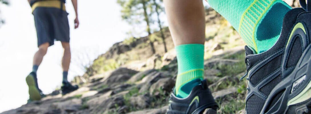 Wanderer mit grünen Trekkingsocken laufen einen Berg hoch	 Zoom auf die Socken