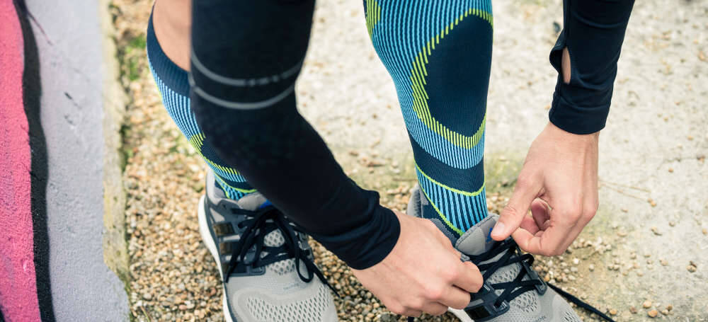 Mann mit grau-blauen Laufsocken schnürt seine Laufschuhe