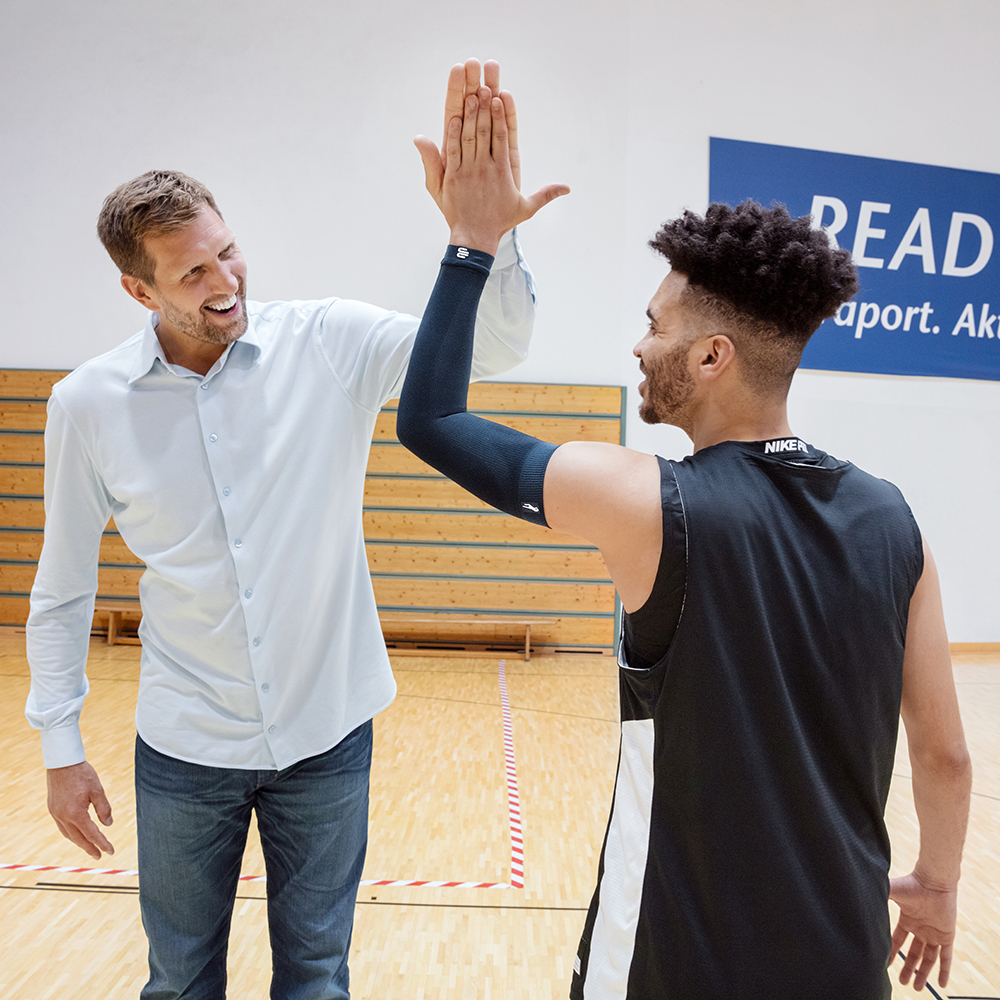 Dirk Nowitzki und ein Basketballspieler der den Arm Sleeve der Dirk Nowitzki Edition trägt klatschen sich ab