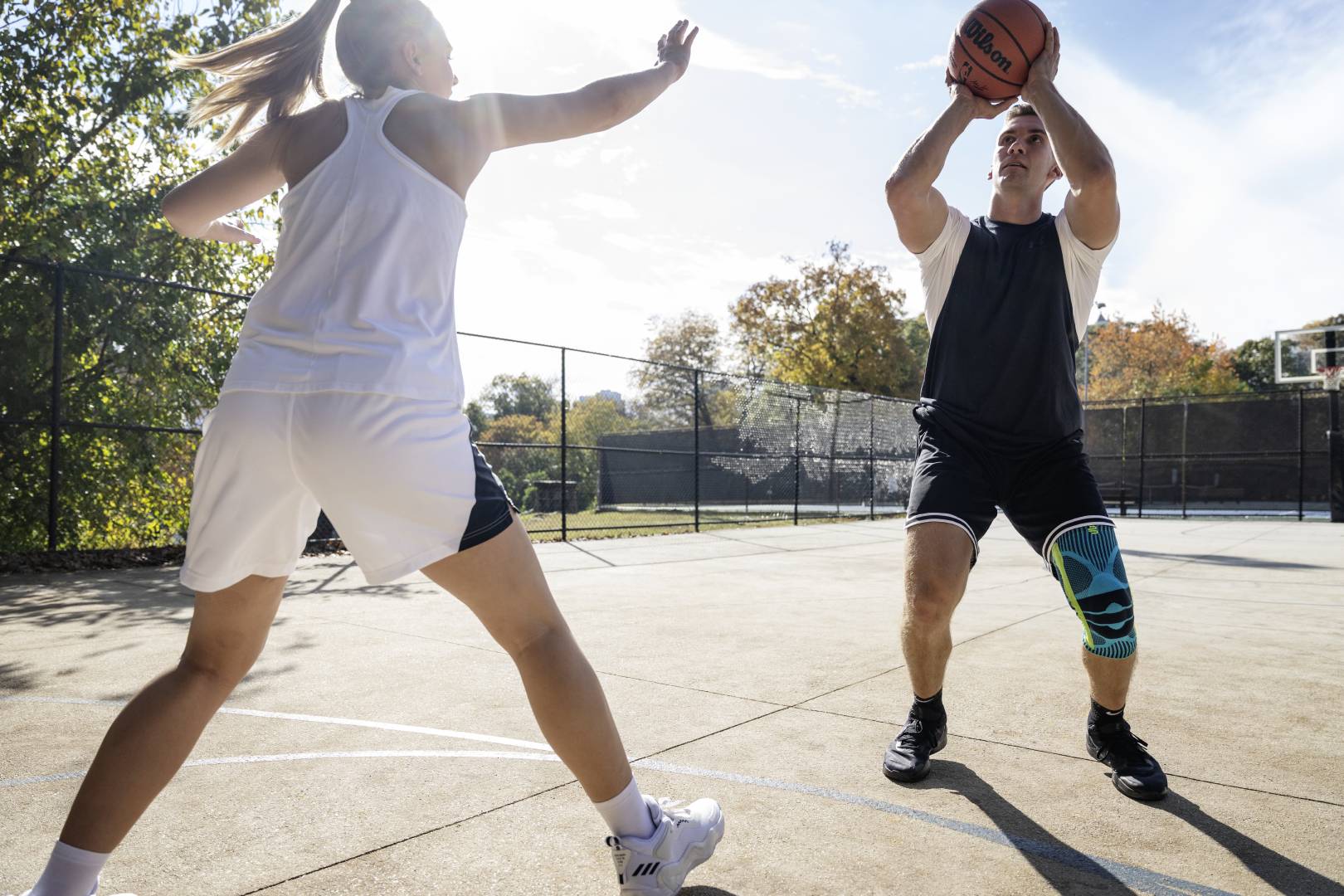 Basketballer mit Kniebandage setzt beim Streetball zum Wurf an	 während seine Gegnerin ihn zu blocken versucht