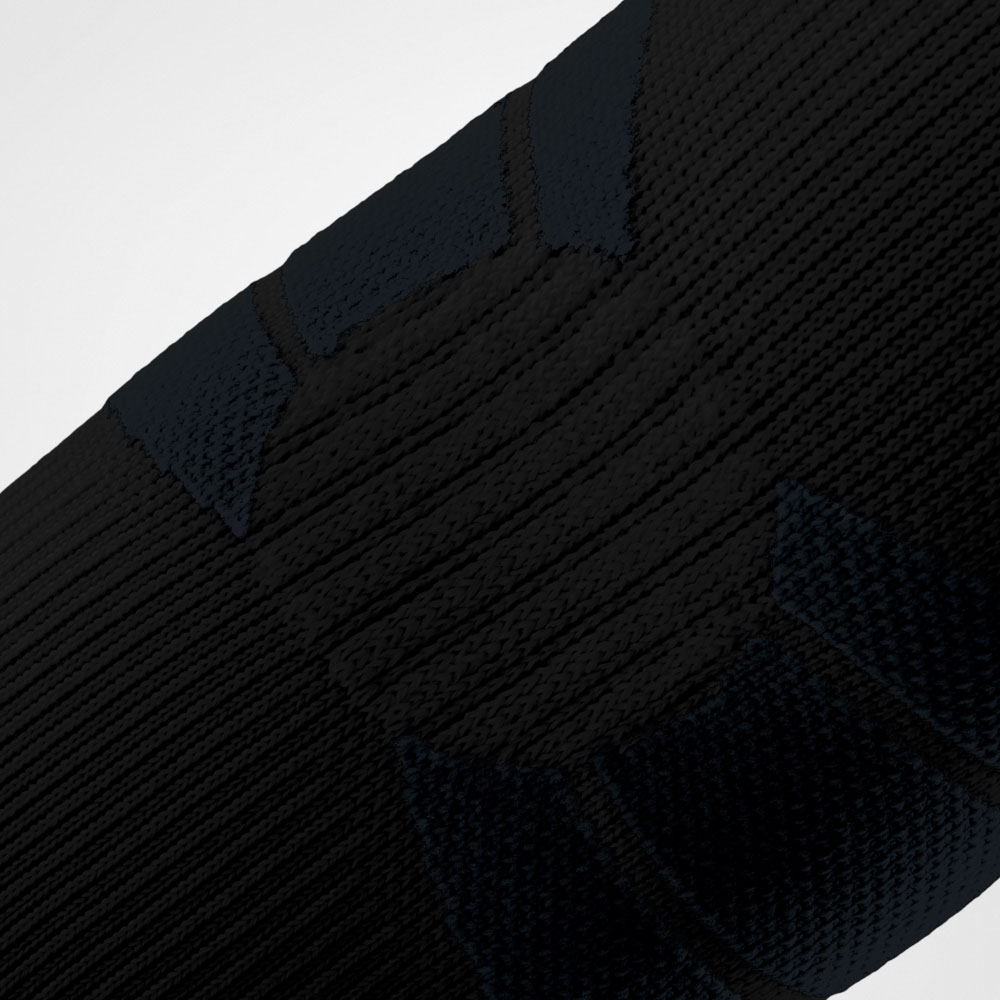 Detailaufnahme der schwarzen Outdoor Compression Elbow Support, die den Ellbogen umschließt. Die feine, technische Strickstruktur mit gezielten Kompressionszonen ist sichtbar und zeigt die anatomische Passform der Bandage
