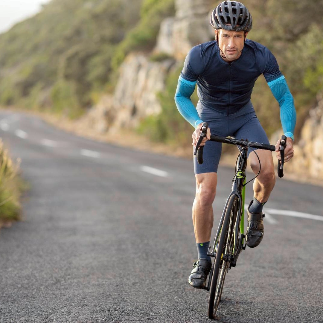 Rennradfahrer auf dem Rennrad der auf einer Straße fährt und dabei blaue Arm Sleeves trägt