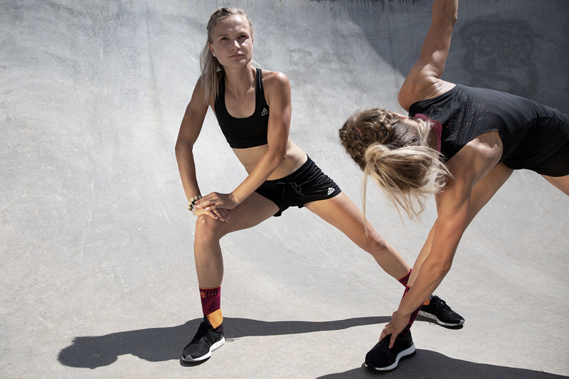 Zwei Sportlerinnen in sommerlichem Outfit stretchen sich in einer Betonpipe