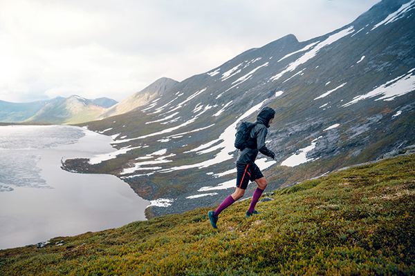 Trailrunner läuft einen grasbewachsenen Berg hinauf bei Regenwetter