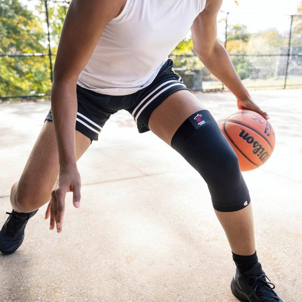 Ein Basketballspieler mit einer schwarzen Miami Heat-Kniebandage in der Defensive. Der Fokus liegt auf der Knieunterstützung beim schnellen Richtungswechsel.