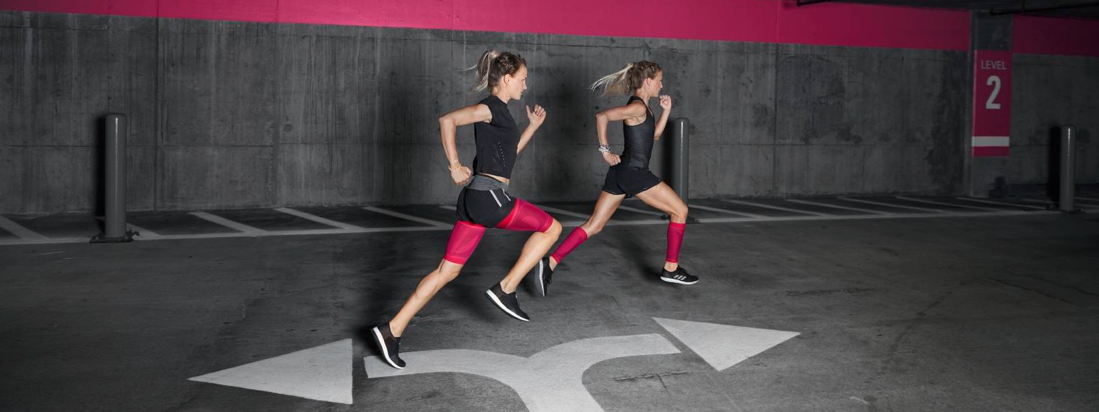 Kräftiger Farbakzent für kraftvolle Muskeln - unsere pinken Compression Sleeves Zwei Läuferinnen mit pinken Compression Sleeves rennen durch ein Parkhaus