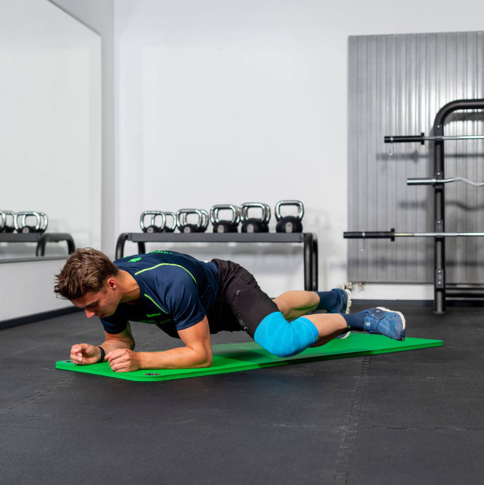 Mann im Fitnessstudio bewegt sein linkes Knie nach vorn bei einem Unterarm Plank