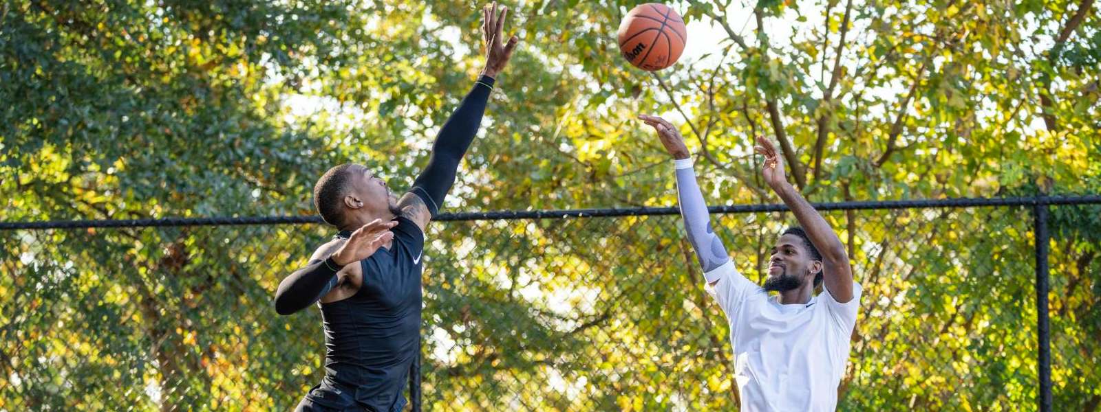 ein Basketballer wirft ein anderer blockt Basketballer in schwarzer Spielkleidung versucht Wurf seines Gegners in weißer Kleidung hoch über dem Boden zu blocken