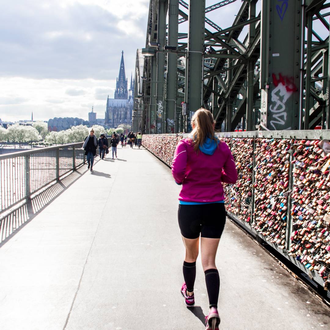 Frau joggt über Kölner Rheinbrücke und trägt schwarze Wadenstulpen