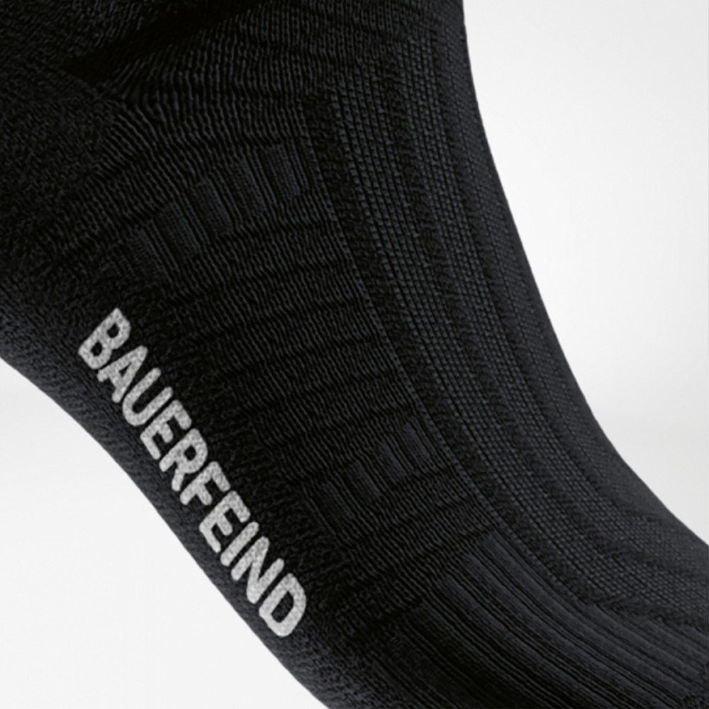 Nahaufnahme des Spannbereichs einer schwarzen Kompressions-Laufsocke mit eingestricktem BAUERFEIND-Logo und strukturierter Oberfläche für optimalen Halt.