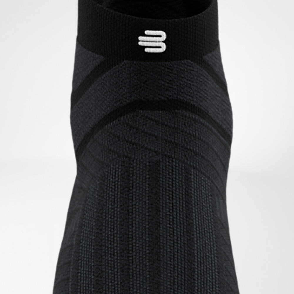 Leichtfüßig durchstarten in Schwarz Schwarze Run Performance Low Cut Socke von Bauerfeind in Frontalansicht, die den Fußrücken mit eingearbeitetem Funktionsmuster und das elastische Bündchen mit weißem Logo zeigt.