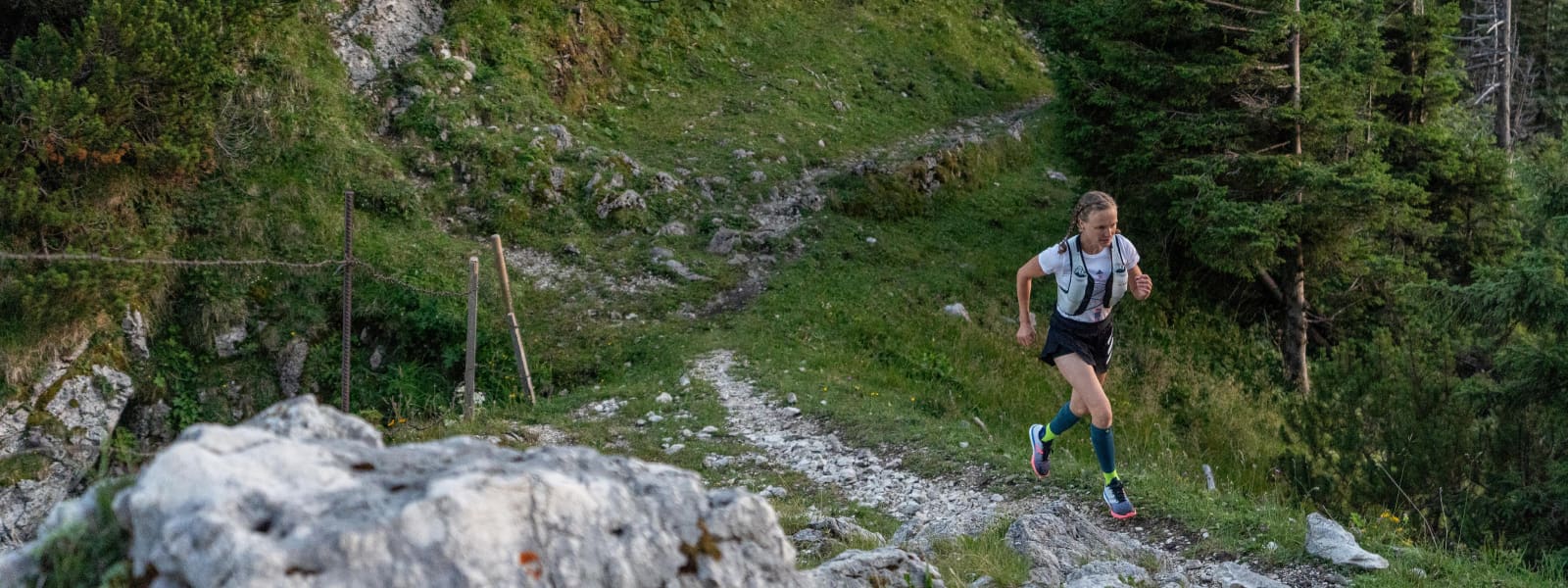 Läuferin hat Trail Run Socken an und joggt über ein steiniges, hügeliges Gelände im Wald