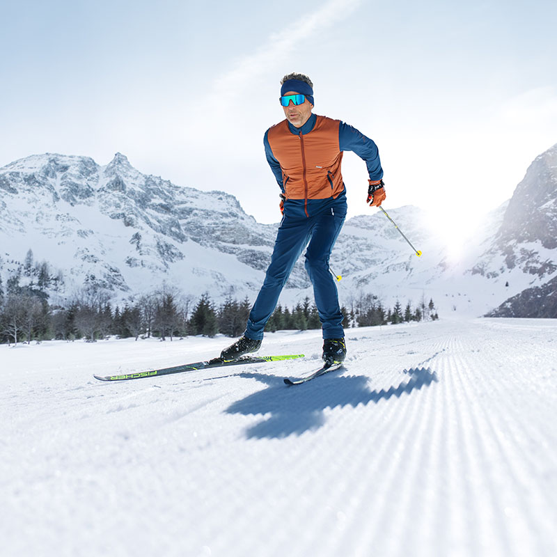 Abenteuer auf der Piste: Skifahrer im Winterlook Ein Mann mit blauer Skibrille, frontal fotografiert, fährt gerade in einer Winterlandschaft Ski. Er trägt dabei eine orangefarbene Jacke und eine blaue Skihose.