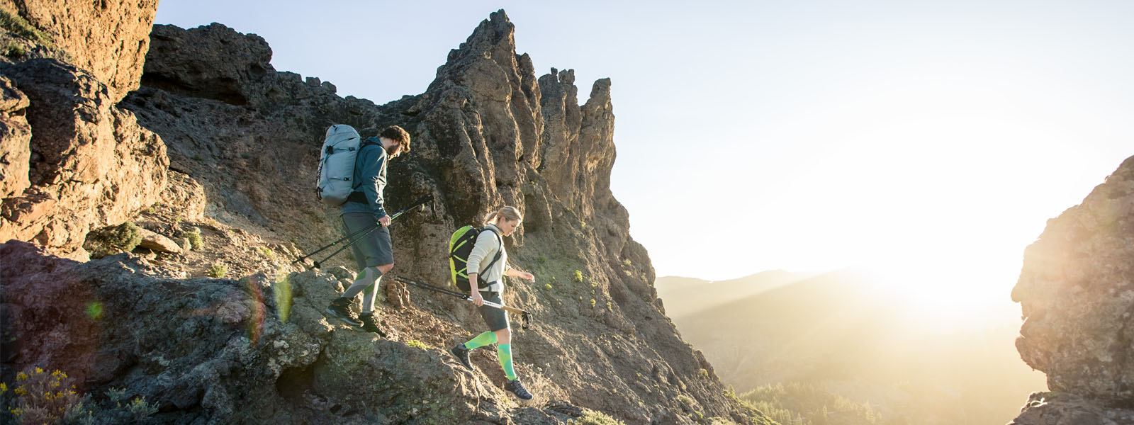 Wanderfreude bis zum Sonnenuntergang: Unsere Outdoor Performance Compression Socks Zwei Wanderer mit langen Wandersocken gehen in der Dämmerung einen steilen Weg an einem Berg herunter