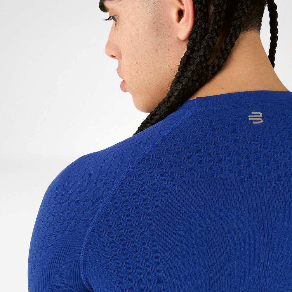 Rückansicht eines Athleten in einem blauen Kompressionsshirt mit strukturiertem Gewebe und geflochtenen Haaren.