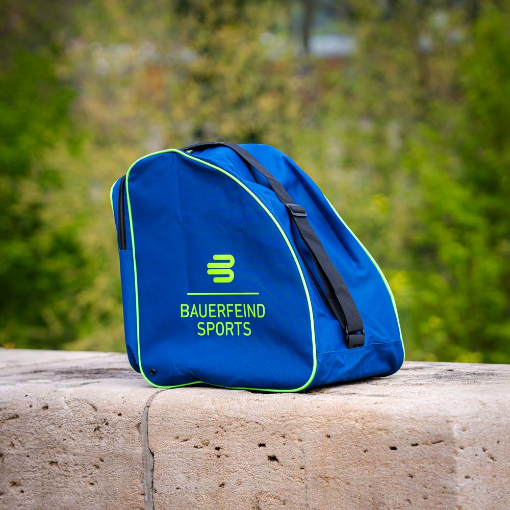 Bauerfeind Sports Tasche Outdoor Eine blaue Tasche mit Bauerfeind Sports Logo, auf einem steinernen Hintergrund draußen fotografiert. Die Tasche hat grüne Akzente und schwarze Riemen.