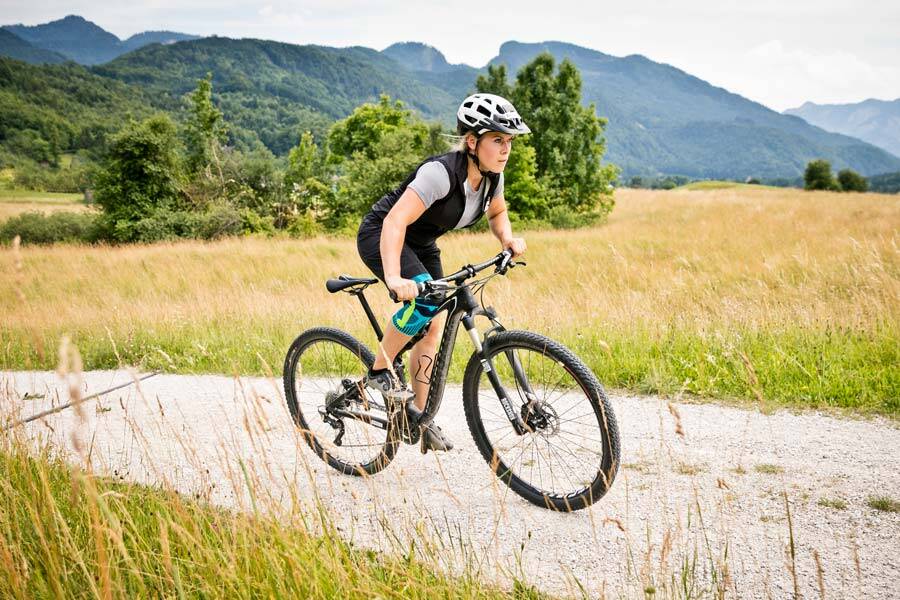 Frau mit Kniebandage fährt auf ihrem Mountainbike über einen Kiesweg zwischen Wiesen und Feldern