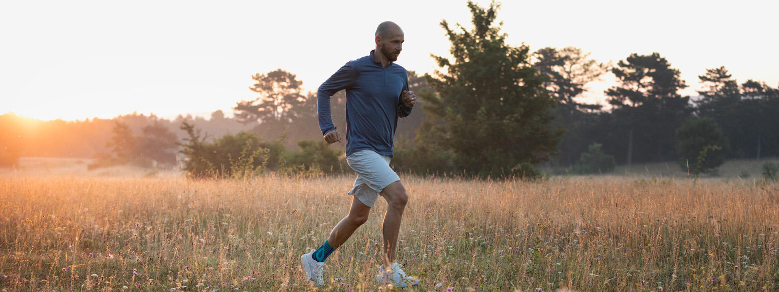 Achillessehnenschmerzen beim Laufen den Kampf ansagen - mit unsere Sports Achilles Support Mann mit Sprunggelenkbandage läuft in der Dämmerung über eine Wiese mit hohem Gras