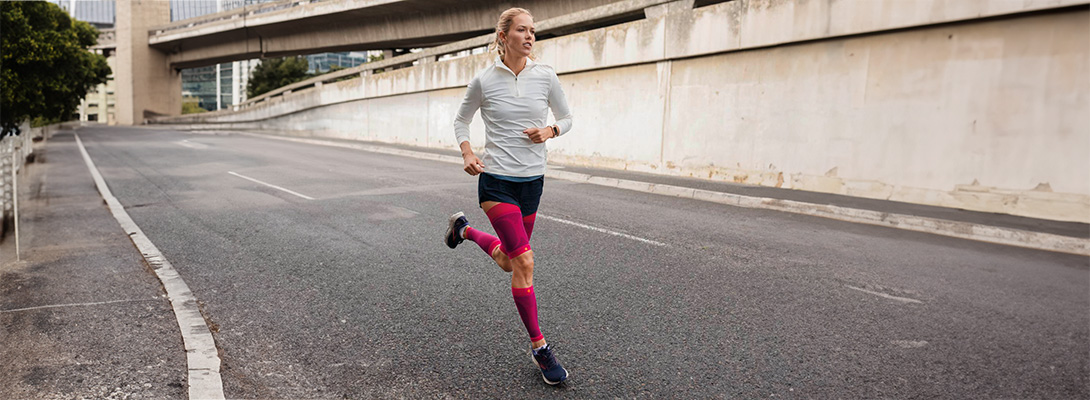 Waden Sleeves beim Laufen Läuferin mit pinken Sleeves läuft durch die Stadt
