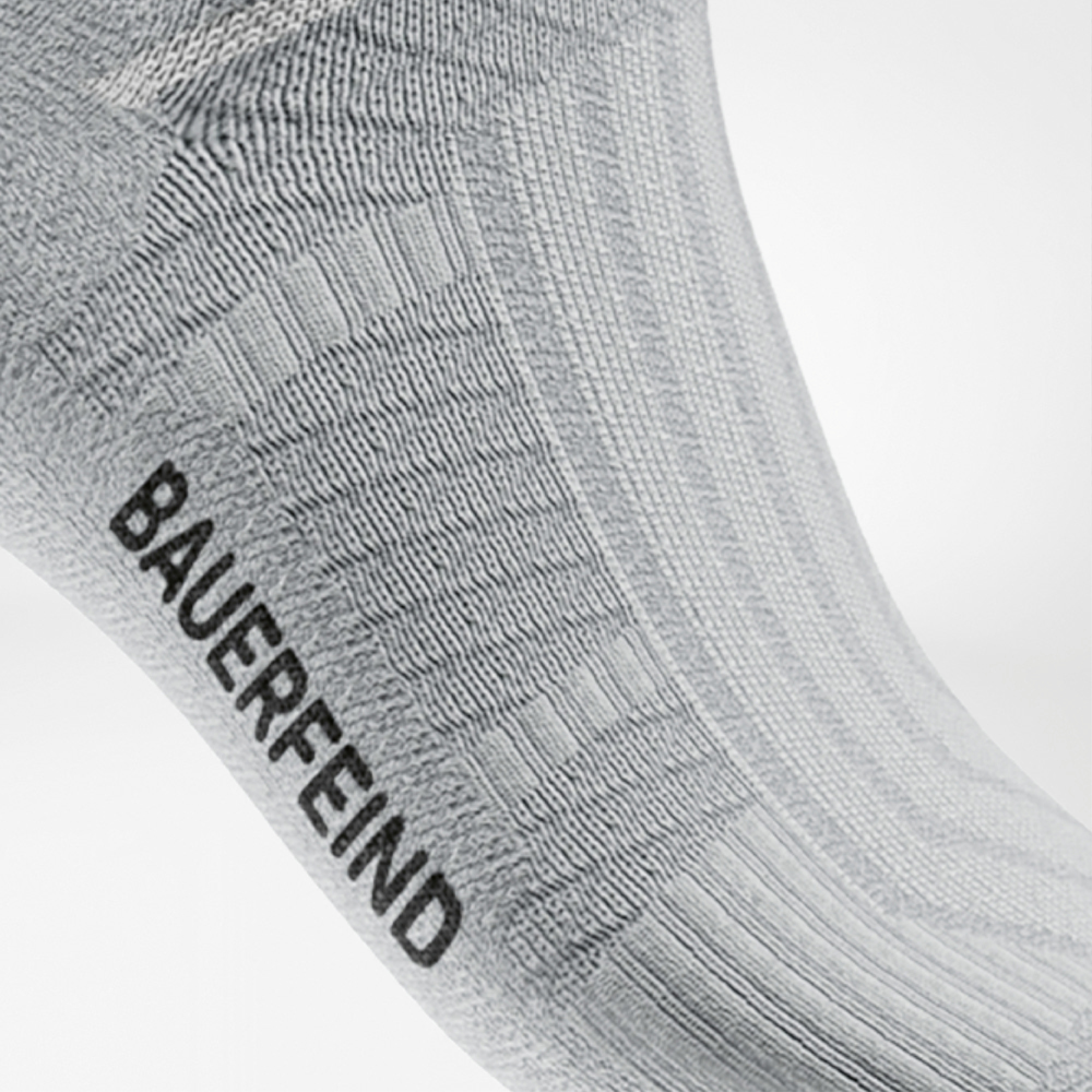 Detailaufnahme einer weißen Midcut-Laufsocke von Bauerfeind mit markanter Rippstruktur und eingestrickter Stützzone am Fußgewölbe. Das Material zeigt eine atmungsaktive, nahtlose Verarbeitung, die für hohen Tragekomfort und Stabilität beim Laufen sorgt.