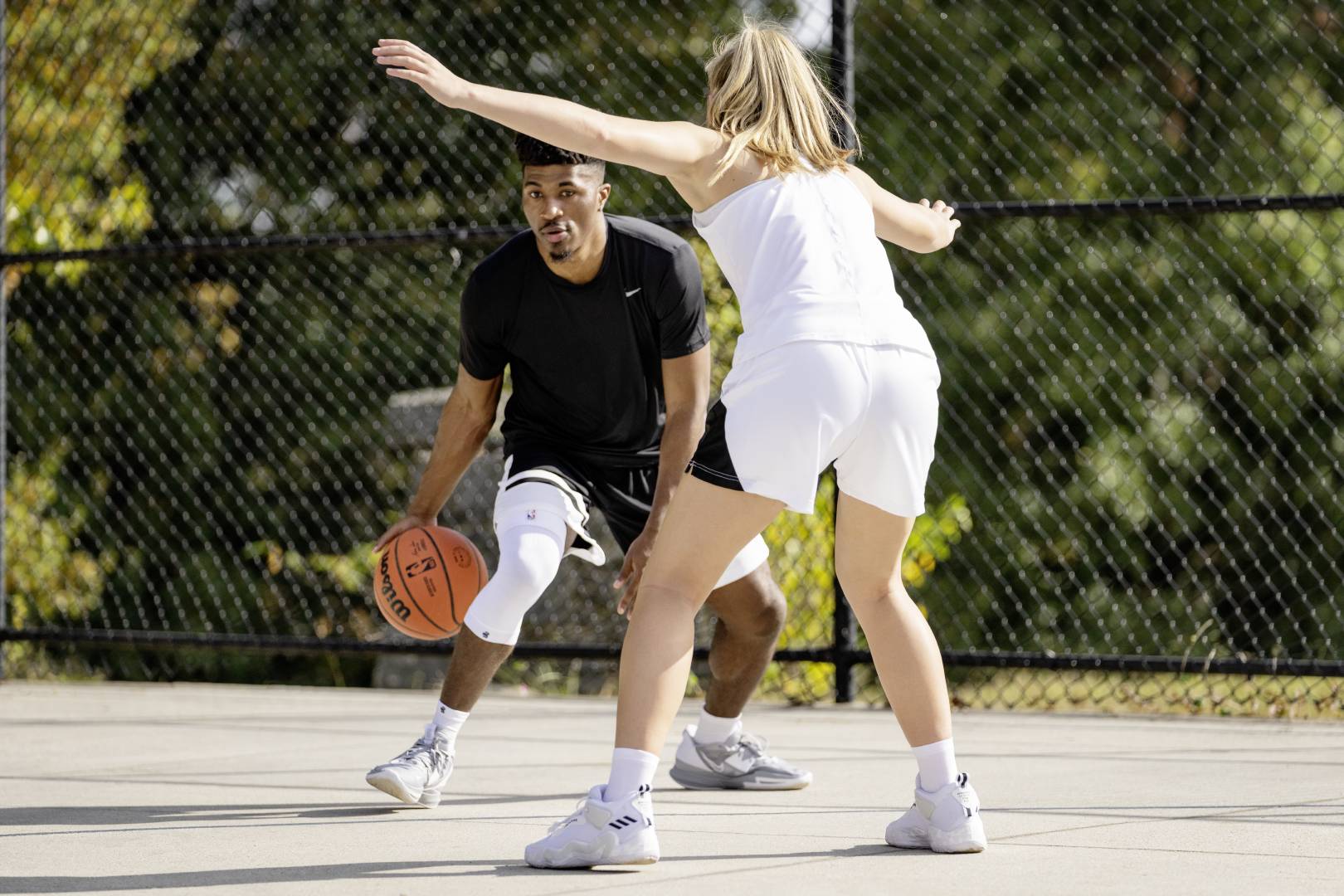 Streetballspieler mit weißem Knee Sleeve versucht beim Dribbling an einer Gegenspielerin vorbeizukommen	 die mit ausgebreiteten Armen auf ihn wartet