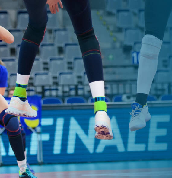 Volleyballerin mit dunklen Hosen	 weißen Schuhen und blauen Sprunggelenkbandagen "steht" in der Luft