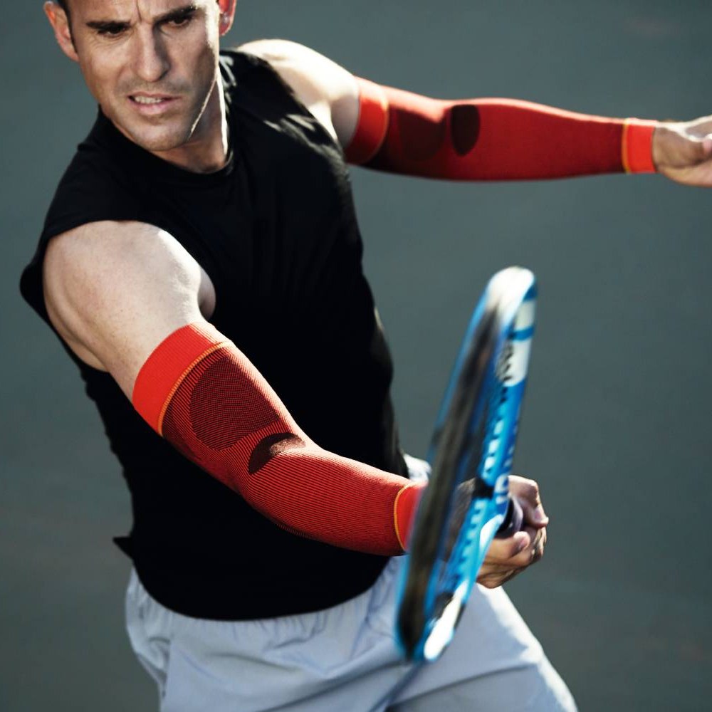 Ein Tennisspieler mit roten Kompressionsärmeln schlägt einen Ball mit intensiver Konzentration.