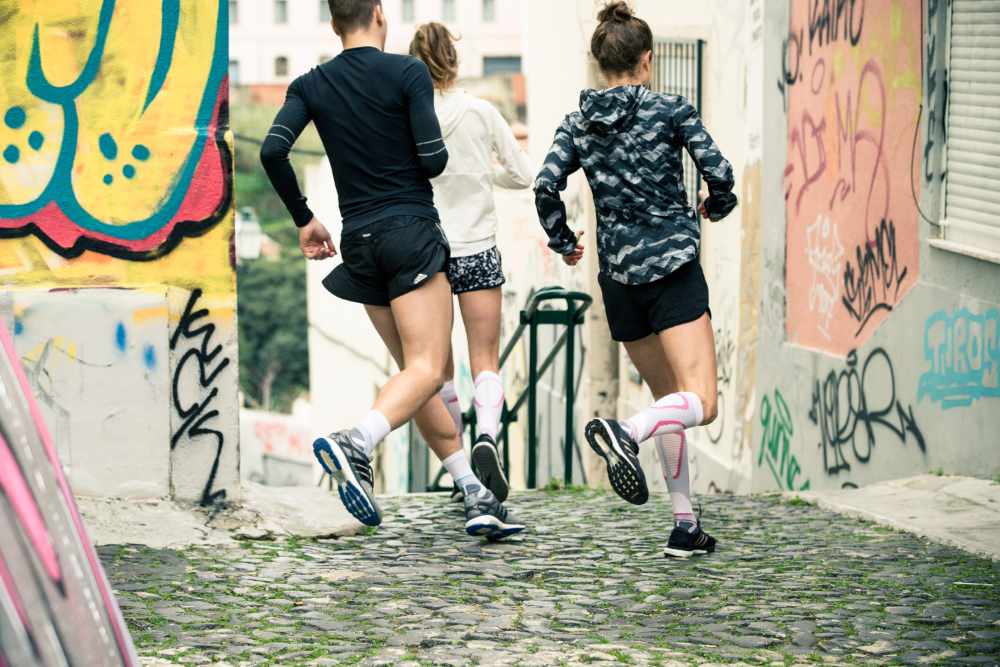 Gruppe aus drei Läufern läuft um eine Ecke in einer Altstadt mit Graffitis an den Wänden auf eine Treppe zu