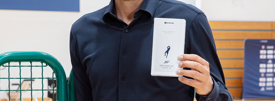 Dirk Nowitzki zeigt die Verpackung des Knee Sleeves der Dirk Nowitzki Edition in die Kamera