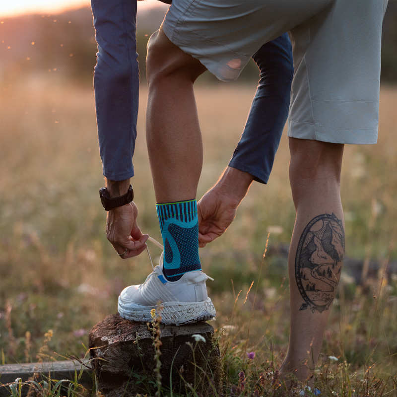 Mann mit Fußbandage bindet Laufschuh mit seinem Fuß auf einem Baumstumpf