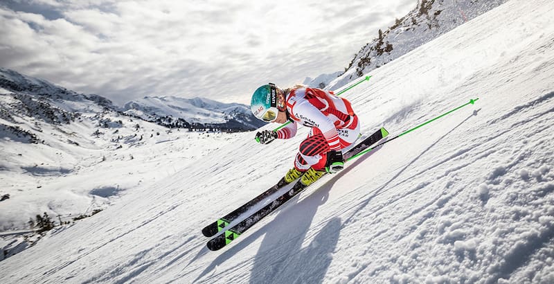 Skifahrerin im rot-weißen Rennanzug in extremer Schräglage auf der Abfahrt