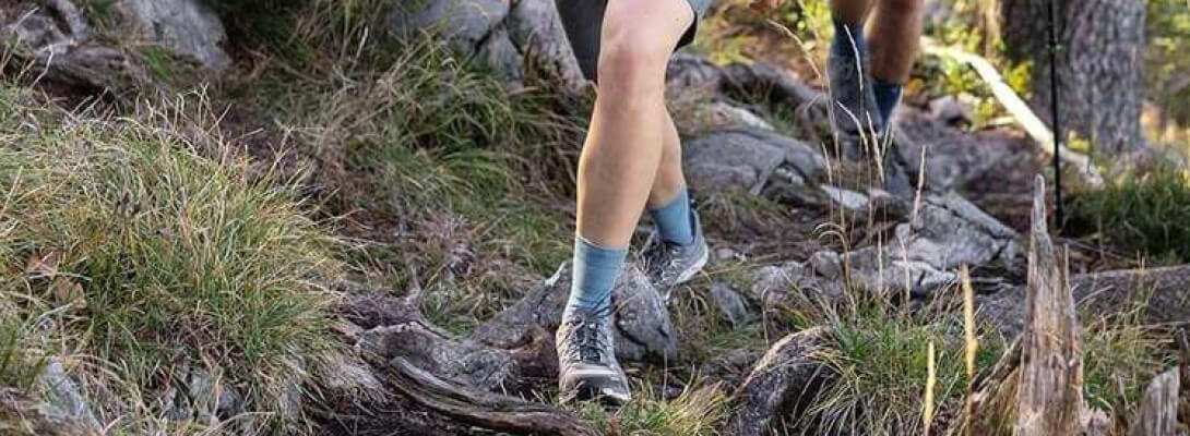 Mittellange Merino-Wandersocken beim Wandern im Wald Wandernde Frau auf steinigem Untergrund trägt mittellange Wandersocken