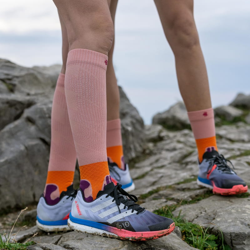 Rosa Mittellange und Kompressionssocken der Trail Run Socke von Bauerfeind Sports auf einem Felsen 